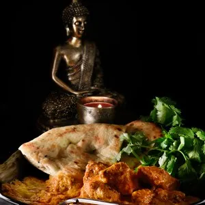 Creatively lit Indian chicken tikka masala meal with fresh coriander or cilantro herbs against a dark background. Generous accommodation for copy space.