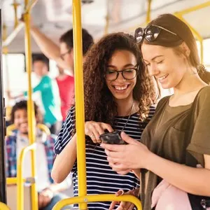 Two friends laughing and watching phone while waiting for bus to depart