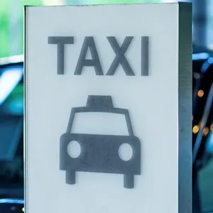 Taxi is waiting for customer behind a taxi stand sign in the front of a hotel
