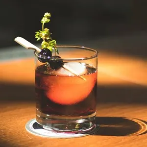 brown beverage with olives and herb in rocks glass