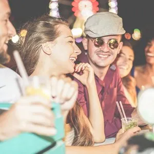 Group of happy friends drinking cocktails and laughing at beach party outdoors