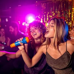 Friends enjoying karaoke night, singing in a nightclub with colorful lights and shiny decorations