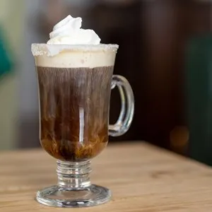 A clear glass mug of Irish coffee with whipped cream and a sugar rim.