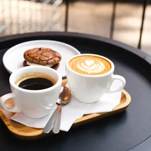 A cup of coffee and a cup of cappuccino with chocolate chip cookies on a table