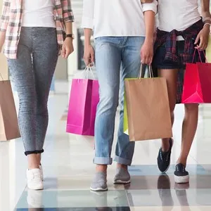 Three consumers with paperbags walking down shopping center