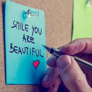 Romantic boyfriend writing Smile you are beautiful message on a blue post it paper with a vintage style filter effect.