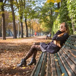 Portrait of young blonde woman relaxing listening to music with headphones outdoors in a park in autumn. Ducale Park - Parma, Italy.