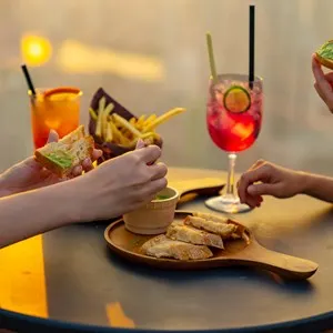 friends celebrating dinner party together at skyscraper rooftop restaurant bar in the city at summer sunset.