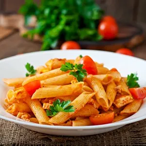 Penne pasta in tomato sauce with chicken, tomatoes decorated with parsley on a wooden background