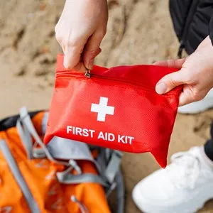 A person attentively packs a first aid kit into a backpack for travel or recreation, including personal protective equipment.