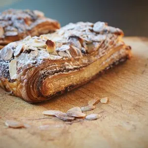 Fresh chocolate and almond croissant pastry, sprinkled with icing sugar on a brown wooden serving board with copy space - Shallow Depth of Field (DOF) - Image