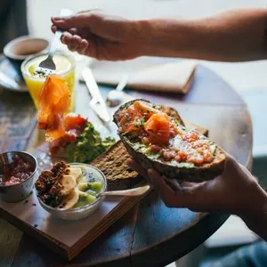 Young man enjoys big and tasty breakfast at downtown cafe, prepares delicious sandwich or toast with avocado spread and smoked salmon on top. chia seeds with yoghurt for dessert
