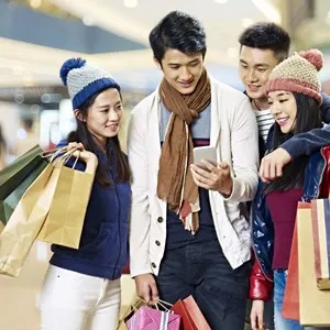 two asian couples using cellphone and sharing information while shopping for christmas in mall or department store