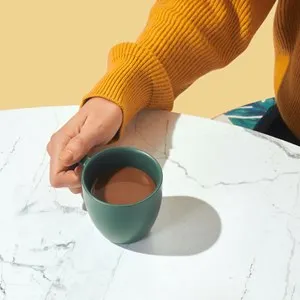 person in a knitted sweater holding a coffee cup on a marble table