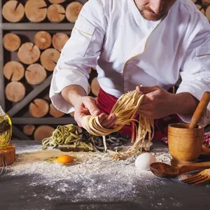 Male chef making homemade pasta with flour and eggs over old wooden table