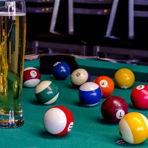 Colorful billiard balls sitting on pool table with glass of beer