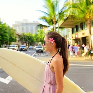 girl holding surf board crossing street to go to the beach