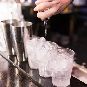 bartender makes a cocktail pouring alchool inside the glass