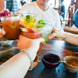 Friends toasting, saying cheers holding tropical blended fruit margaritas. Watermelon and passionfruit drinks.