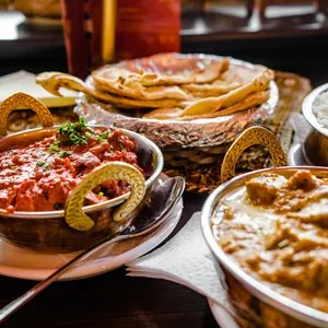 Indian Food or Indian Curry in a copper brass serving oriental bowl, pieces of chicken fillet in curry sauce ingredients in a pan with the old table side view close-up