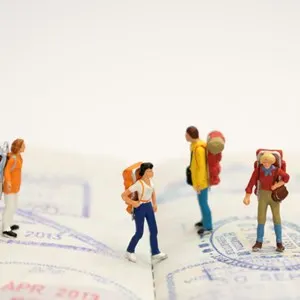 Miniature figurine of young traveler standing on visa stamps , travel concept