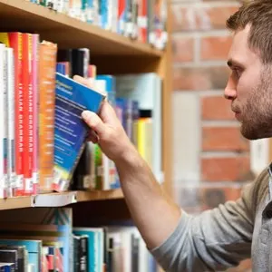 Male student picking a book in a library