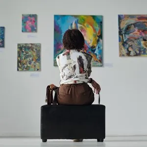 Rear view of young woman sitting on couch and looking at paintings on the wall
