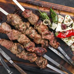 Traditional Greek Souvlaki with Feta and Vegetable as top view on an old burnt cutting board