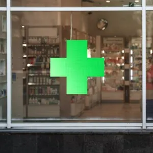 Green cross sign with neon light mounted on pharmacy shop window case outdoor