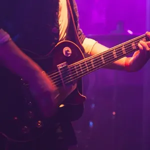 Electric guitar player on stage with purple scenic illumination, soft selective focus