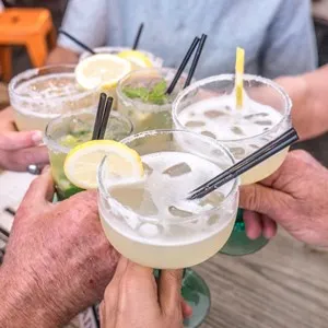 friends making a toast and clinking cocktail glasses with margaritas and mojito
