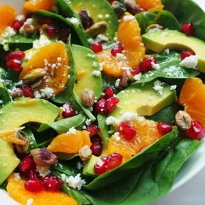 close up view of spinach, avocado salad with orange, pomegranate and pistachio in white bowl on marble background