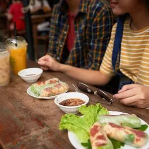 Cropped image of couple eating spring rolls and drinking cocktails.