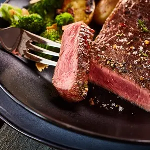 Cropped close up on cut of medium rare cooked beef steak on fork in plate with broccoli