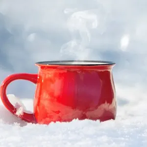 red ceramic cup with hot tea stands on the snow