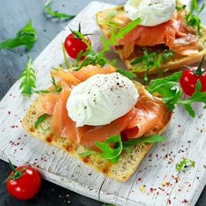 Poached egg on grilled toast with smoked salmon, rucola and vegetables on white board. healthy breakfast