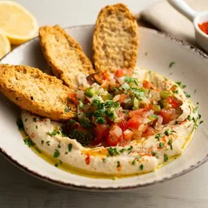 Traditional chickpea hummus with cut pepper and onion in the center served with toast