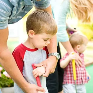 Family: Man Helps Child Hold Putter For Mini-Golf