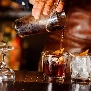 Barman pouring fresh alcoholic drink into the glasses with ice cubes on the bar counter - Image