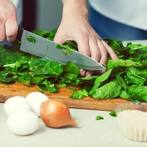 Vegetarian bakery concept. Chef's hands cutting spinach salad in kitchen of cafe, restaurant. Close up. Indoor shot