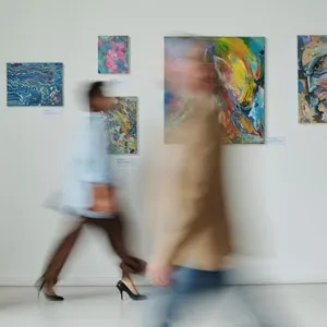 Blurred motion of people visiting art gallery, they walking along the hall among paintings on the wall