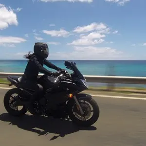 Female biker, dressed in all black, riding bike on a sunny day with blue skies on the west coast of Oahu, Hawaii