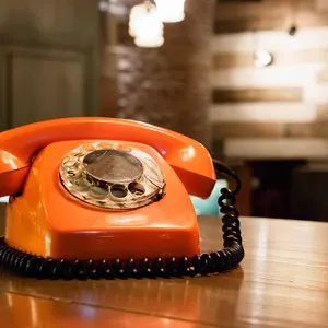 A vintage plastic orange telephone with dial placed on a wooden table inside a bar.