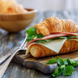Croissant with cheese, ham,cucumber and parsley on a wooden stand.