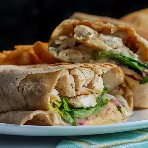 Chicken Caesar salad wrap sandwich with romaine lettuce and french fries.