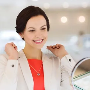 happy woman choosing and trying on pendant at jewelry store