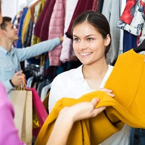 Cheerful female assistant serving customer asking in clothing boutique