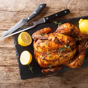 Traditional rotisserie chicken served with lemon closeup on a slate board on a table