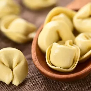 Raw cheese filled tortellini pasta on wooden spoon, photographed with natural light (Selective Focus, Focus on the first tortellini on the spoon)