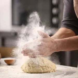 Male hands clapping and sprinkling white flour over dough on kitchen background